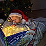 Célia participe au concours pour gagner de l'argent avec cette photo : baby, blanket, book, child, christmas, christmas_tree, curious, cute, decorations, face, fairy_lights, festive, floor, holiday, indoors, santa_hat, soft_lighting, toddler, toy, warm