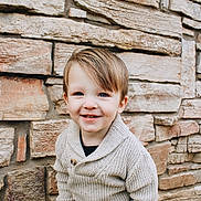 Beckett joined the competition — help win amazing prizes! toddler, child, smiling, sweater, knitted, stone_wall, outdoor, portrait, cute, happy, person, young_child, fashion, casual_clothing, standing, background, texture, natural_light, fall_leaves, photography