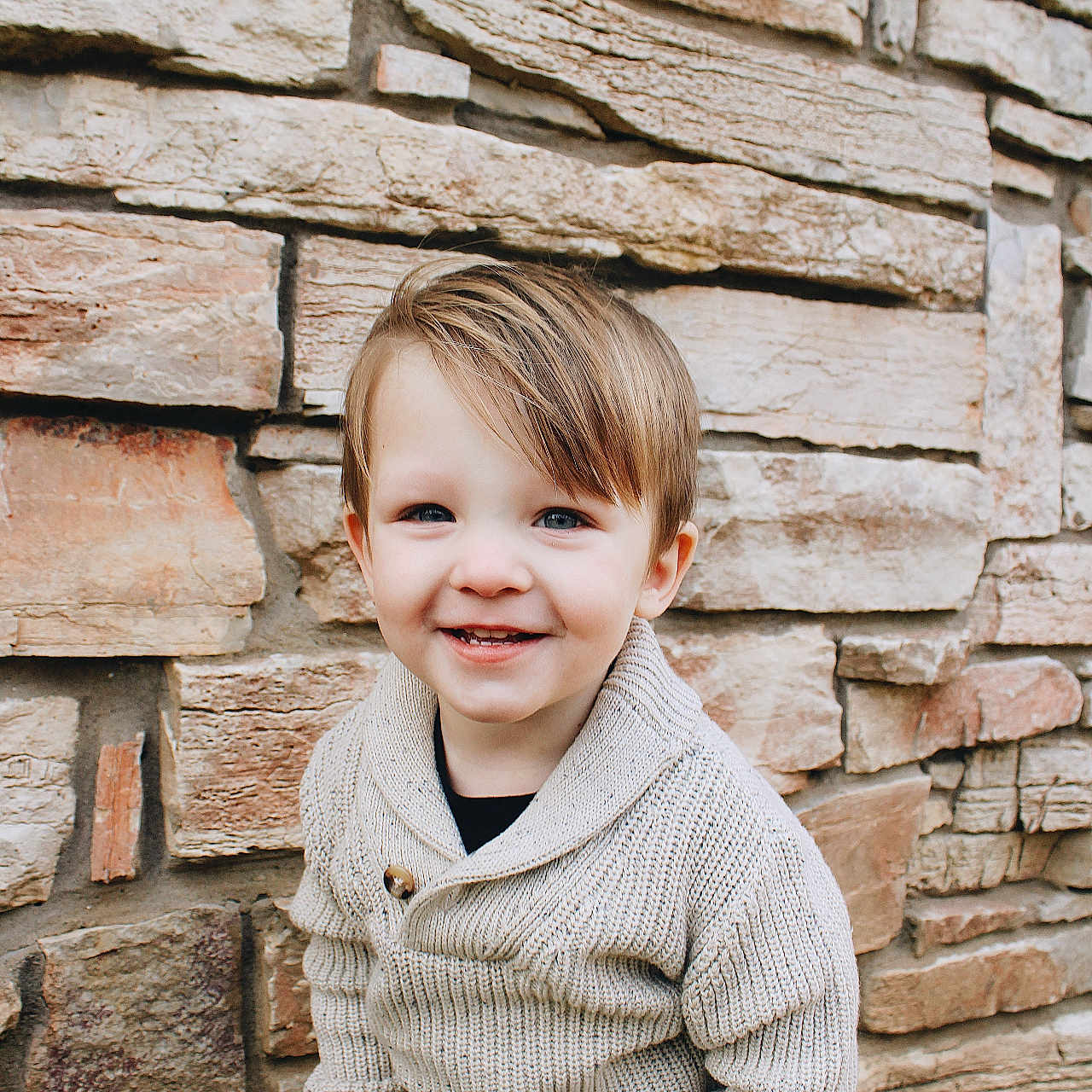 Beckett joined the competition — help win amazing prizes! toddler, child, smiling, sweater, knitted, stone_wall, outdoor, portrait, cute, happy, person, young_child, fashion, casual_clothing, standing, background, texture, natural_light, fall_leaves, photography