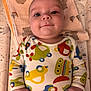 baby, infant, onesie, colorful_clothing, car_print, blanket, patterned_blanket, cute, smiling, lying_down, child, young_child, face, hands, blue_eyes, indoor, soft_lighting, bed, comfort, happy