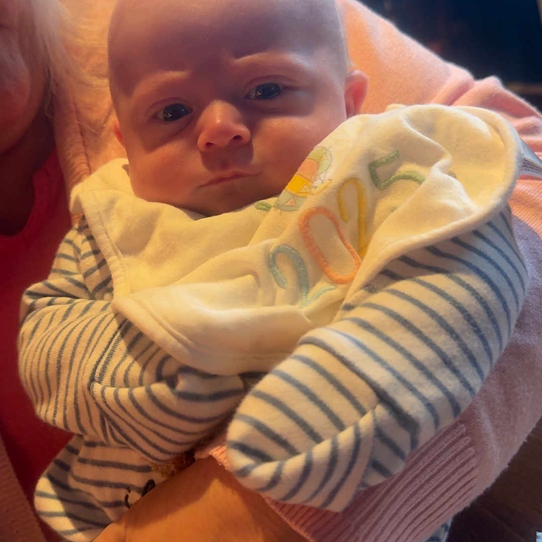 Riley-Jay joined the competition — help win amazing prizes! adult, baby, bib, child, closeup, cozy, face, hand, holding, indoor, infant, natural_light, person, pink_sweater, portrait, serious_expression, soft_light, striped_clothing, warm, window