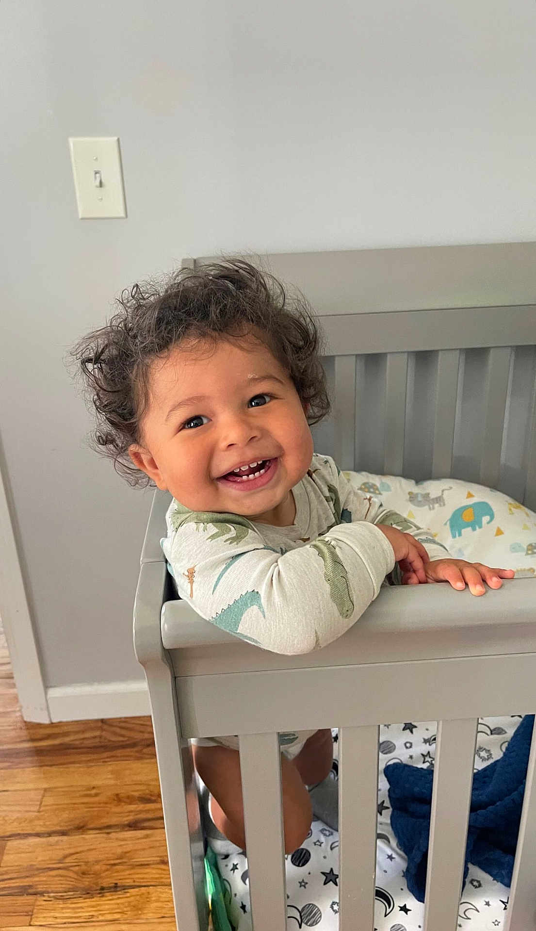 Crew joined the competition — help win amazing prizes! toddler, child, crib, smiling, curly_hair, onesie, dinosaur_print, baby, indoor, wooden_floor, bedding, animal_print, happy, face, person, furniture, home, cute, playful, standing