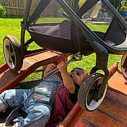 Raven is registered to the contest to win money with this photo: toddler, child, outdoor, grass, stroller, wrench, tool, playground, sunlight, jeans, pink_socks, black_shirt, metal_can, toy, repair, lawn, wheel, daytime, curious, baby