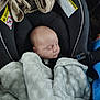 baby, infant, newborn, sleeping_baby, car_seat, blanket, harness, headrest, fabric, soft_texture, warning_label, cozy, child, face, peaceful, portrait, inside_vehicle, seat_belt, clothing, car_accessory