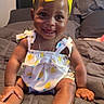 baby, child, smiling, yellow_headband, romper, bed, pillow, blanket, happy, cute, infant, indoors, portrait, sitting, skin, clothing, headwear, person, young_child, home