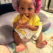 Kinsley is registered to the contest to win money with this photo: baby, child, infant, bonnet, yellow_clothing, ice_cream_cone, play_mat, barefoot, cute, indoor, smiling, sitting, hands, face, headwear, cheerful, soft_toys, colorful, skin, portrait