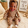 baby, child, smiling, tongue_out, headband, bow, outfit, sitting, rug, teddy_bear, sign, milestone, 5_months, indoor, basket, plant, cozy, cute, portrait, happy