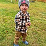 child, toddler, beanie, hat, plaid_shirt, flannel, grass, yard, fence, autumn, leaves, crocs, shoes, portrait, standing, smirk, face, person, outdoor, casual_clothing