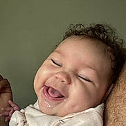 Naomi is registered to the contest to win money with this photo: baby, smiling, laughing, curly_hair, pink_clothing, closeup, face, cheeks, happy, infant, child, skin, person, expression, joy, portrait, indoors, human, cute, toddler