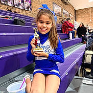 Lyric is registered to the contest to win money with this photo: child, girl, cheerleader, trophy, blue_uniform, bow, bleachers, gym, sports, smile, drink, cup, purple, brick_wall, spectators, basketball, posters, indoor, happy, sitting