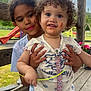 child, toddler, outdoor, playground, bench, smile, curly_hair, holding, clothing, face_paint, happy, nature, grass, wood, person, cute, family, daylight, expression, park