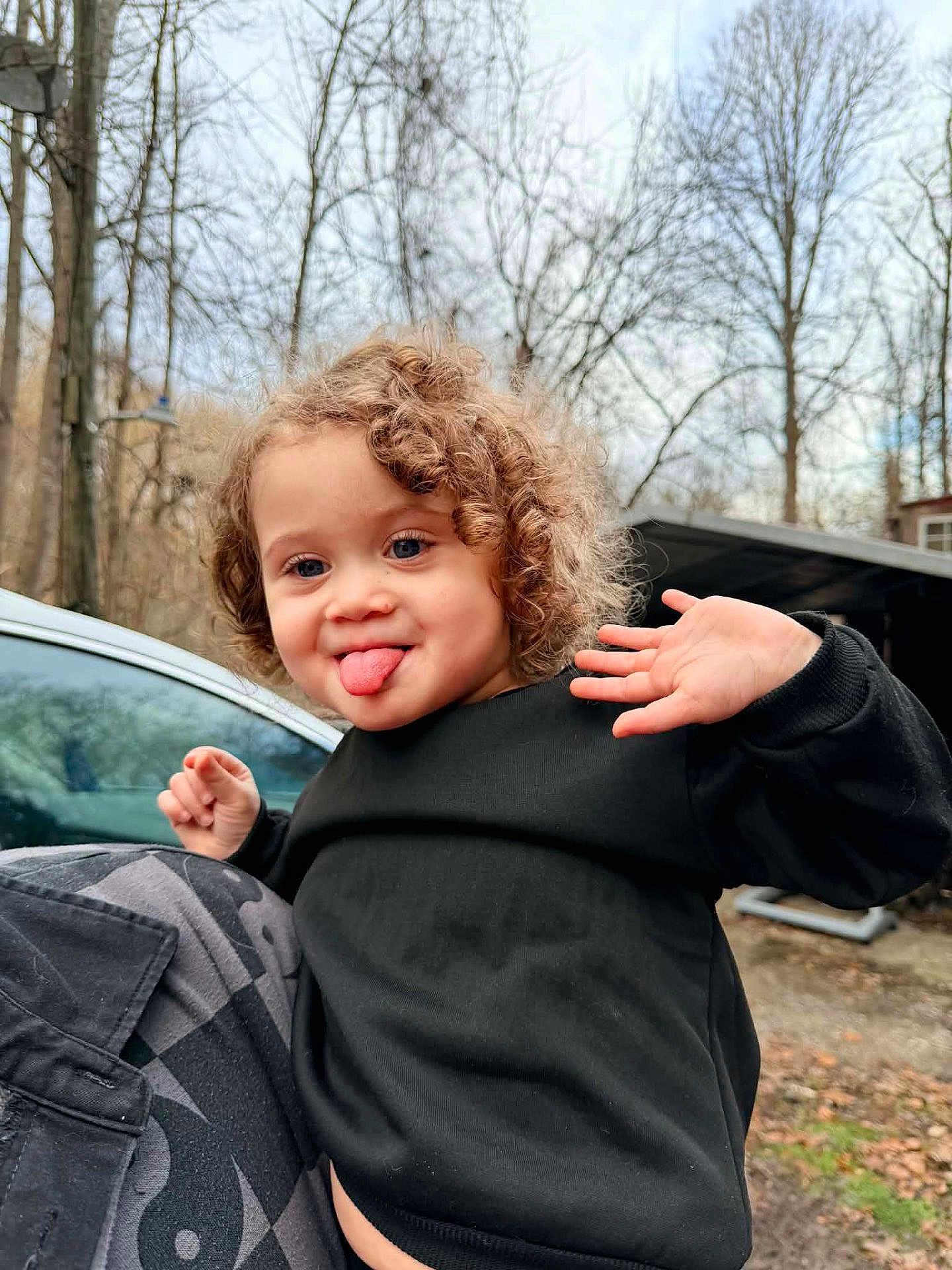 Lydiah is registered to the contest to win money with this photo: autumn, black_sweater, car, child, curly_hair, cute, expression, face, fall, hand_wave, nature, outdoor, person, playful, portrait, smile, toddler, tongue_out, trees, young_child