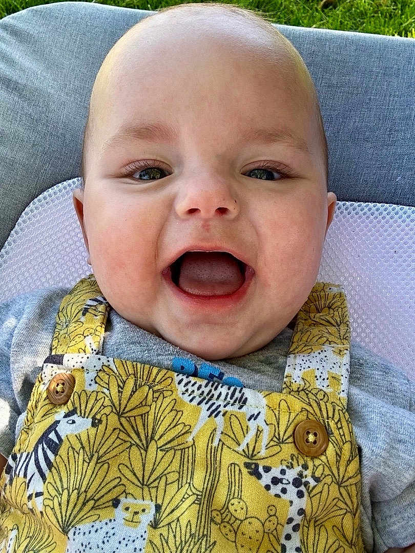 Tobias joined the competition — help win amazing prizes! baby, smiling, face, child, yellow_overall, animal_print, outdoor, grass, cushion, happy, cute, infant, portrait, clothing, button, head, skin, mouth_open, eyes, person