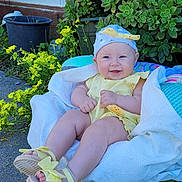 Katrena is registered to the contest to win money with this photo: baby, child, yellow_clothing, blue_hat, sandals, smile, outdoor, plants, flowers, greenery, blanket, sitting, happy, cute, sunny, nature, portrait, infant, face, feet