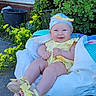 baby, child, yellow_clothing, blue_hat, sandals, smile, outdoor, plants, flowers, greenery, blanket, sitting, happy, cute, sunny, nature, portrait, infant, face, feet