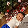 baby, sleeping, blanket, christmas_tree, ornaments, red, white, green, plaid, floor, wooden_floor, clothing, pants, shirt, holiday, festive, indoor, decorations, peaceful, person