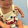 Noah is registered to the contest to win money with this photo: baby, child, smiling, romper, clothing, hand, person, jewelry, necklace, bracelet, sitting, blue_background, closeup, cute, infant, skin, happy, seated, support, indoor
