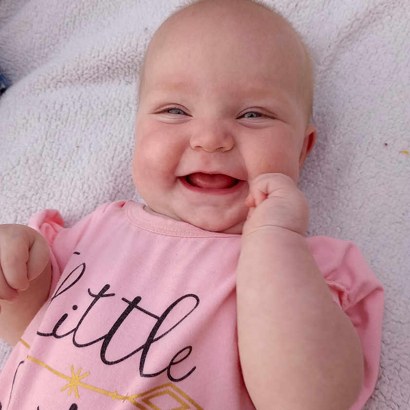 Grace is registered to the contest to win money with this photo: baby, babylaughing, bodypart, clothing, cushion, face, finger, hand, happy, head, laughing, mouth, newborn, person, photography, portrait, smile, t_shirt, teeth, text