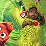 baby, child, costume, green, grinch, blanket, fur, cute, lying_down, floor, headband, expression, portrait, indoor, holiday, character, red_heart, curious, wide_eyes, soft_texture