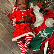 Rain is registered to the contest to win money with this photo: baby, child, christmas, holiday, red_dress, headband, striped_socks, floor, festive, decorations, christmas_tree, ornament, toy, candy_cane_pattern, infant, cute, holiday_outfit, smiling, person, celebration
