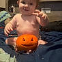 baby, child, pumpkin, jack_o_lantern, bed, blanket, toddler, carved_pumpkin, indoor, portrait, cute, smile, hair, face, halloween, decor, tapestry, furniture, room, expression
