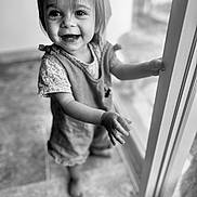 Hanaé participe au concours pour gagner de l'argent avec cette photo : toddler, child, smiling, indoor, black_and_white, portrait, happy, face, hand, glass_door, clothing, floor, person, cute, young_child, expression, window, hair, barefoot, light