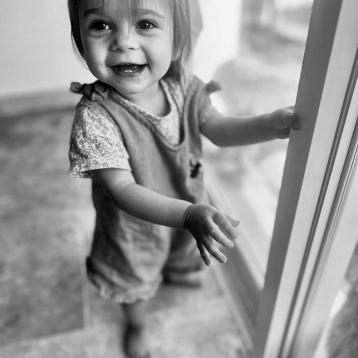 Hanaé participe au concours pour gagner de l'argent avec cette photo : barefoot, black_and_white, child, clothing, cute, expression, face, floor, glass_door, hair, hand, happy, indoor, light, person, portrait, smiling, toddler, window, young_child