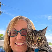 Piper joined the competition — help win amazing prizes! woman, cat, tabby_cat, glasses, smile, outdoor, blue_sky, sun_decoration, happy, pet, face, portrait, holding, feline, animal, person, daylight, nature, closeup, casual