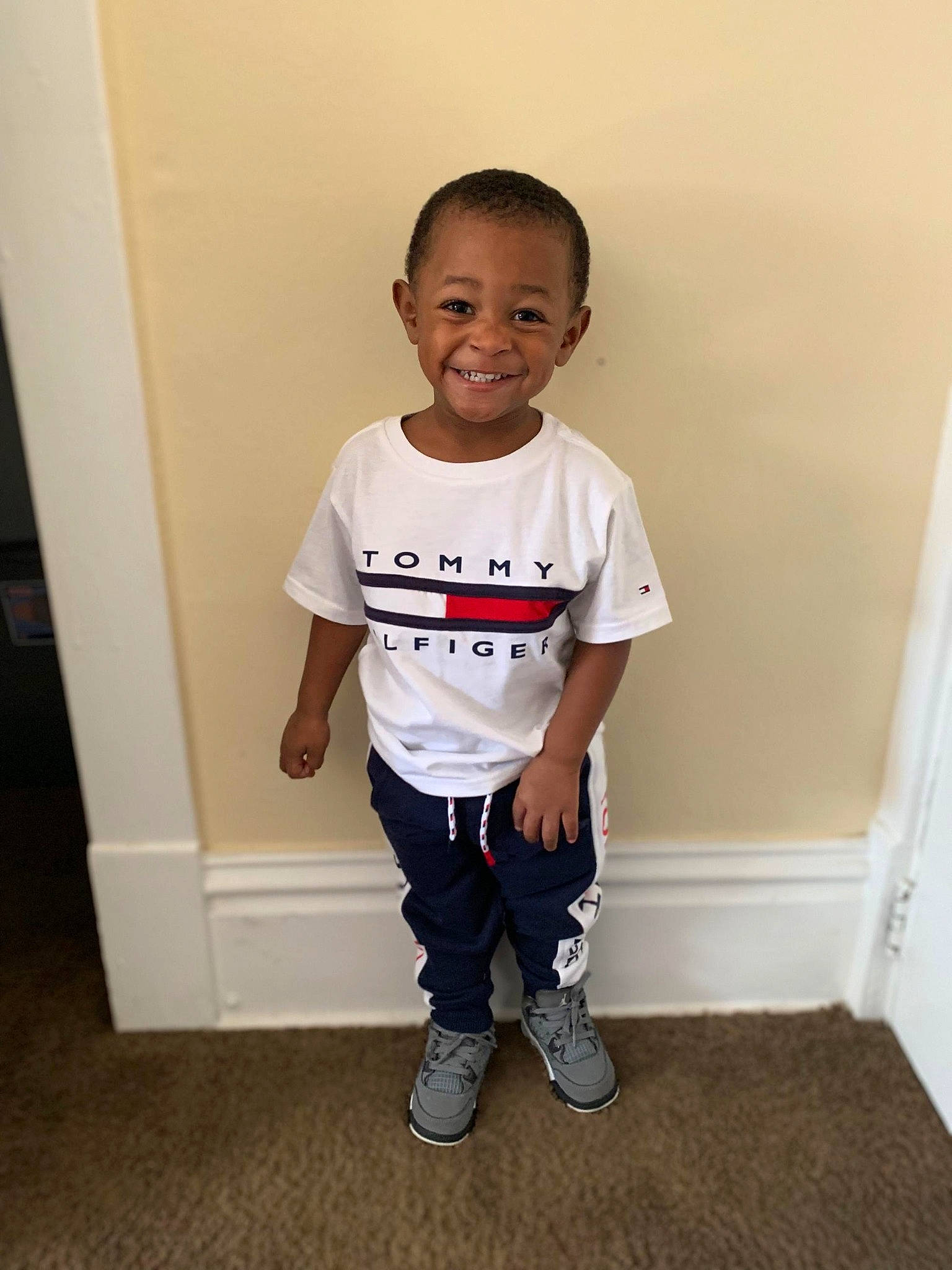 Jontae is registered to the contest to win money with this photo: child, floor, footwear, happy, head, joy, male, person, shoe, shoulder, sleeve, smile, standing, t_shirt, toddler, top, white
