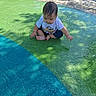 Samuel is registered to the contest to win money with this photo: baby, child, wet, water, sitting, curious, outdoor, playground, colorful, green, blue, toddler, short_sleeves, concrete, shadow, daylight, foot, pavement, person, young