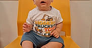 Samuel is registered to the contest to win money with this photo: baby, child, yellow_chair, window, blinds, shirt, sitting, indoor, curious, expression, feet, hands, clothing, person, face, young_child, furniture, floor, looking_up, cute