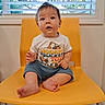 baby, child, yellow_chair, window, blinds, shirt, sitting, indoor, curious, expression, feet, hands, clothing, person, face, young_child, furniture, floor, looking_up, cute