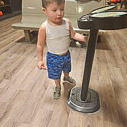 Sabastian joined the competition — help win amazing prizes! toddler, child, indoor, bowling_alley, floor, gaming_machine, tank_top, shorts, sneakers, people, bench, bowling_balls, wood_floor, standing, curious, casual_clothing, young_child, activity, background_people, leisure