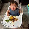 Raven Wright is registered to the contest to win money with this photo: toddler, child, high_chair, bib, food, broccoli, corn, ground_meat, messy_food, kitchen, tile_floor, laundry_basket, indoor, eating, curious, messy_hair, young_child, feeding_time, person, baby