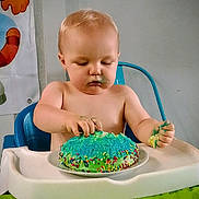 Layken joined the competition — help win amazing prizes! baby, birthday, blue_frosting, cake, child, cute, exploration, expression, face, food, green_tablecloth, hands, high_chair, indoor, messy, person, plate, sprinkles, table, toddler