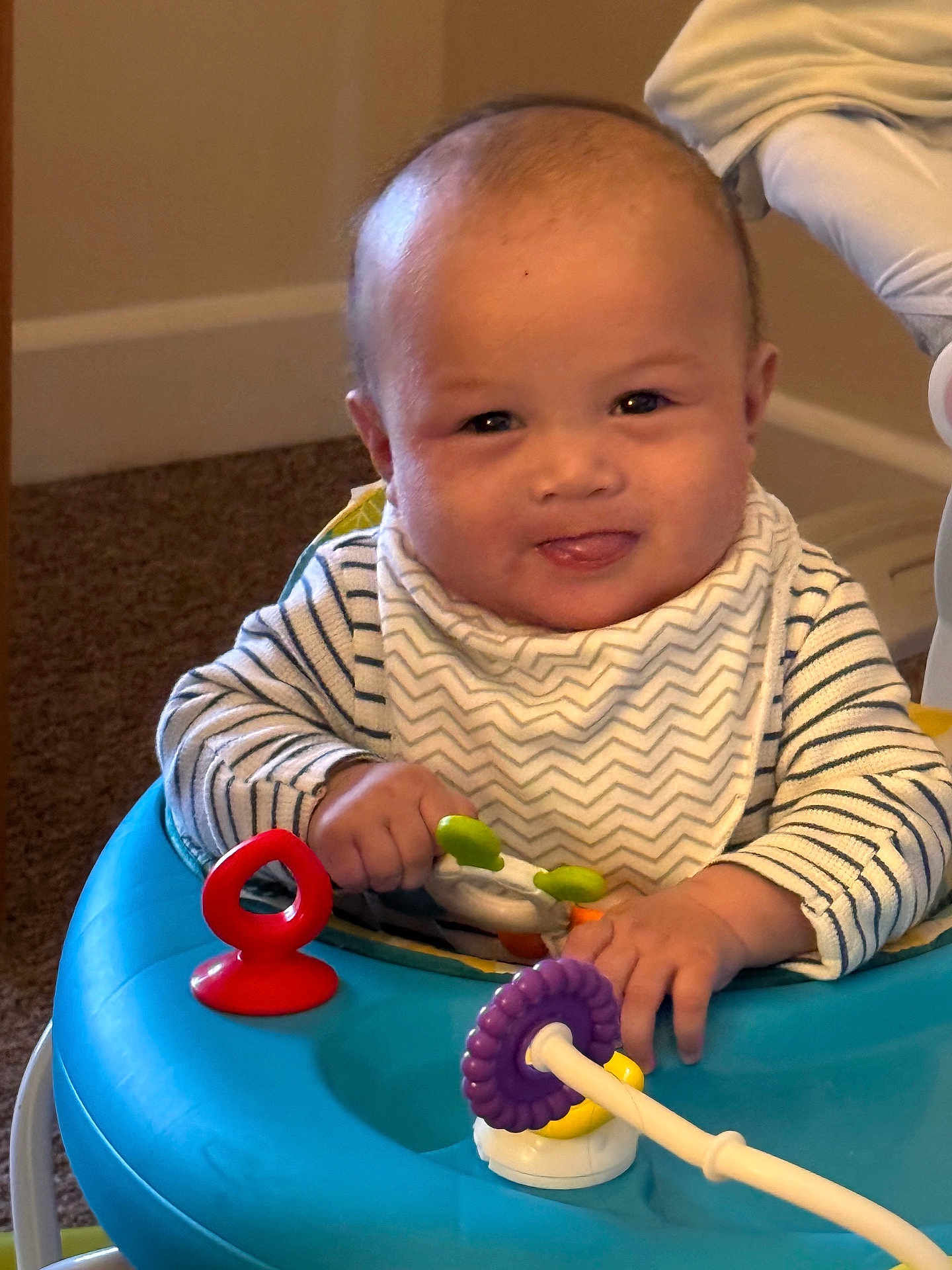 Enzo joined the competition — help win amazing prizes! baby, child, infant, play, toy, activity_center, blue, red, purple, striped_clothing, bib, indoor, carpet, smiling, tongue_out, person, cute, happy, young, hands