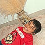 child, smiling, red_shirt, super_mario, carpet, indoor, vase, pampas_grass, decor, happy, boy, casual_clothing, floor, home, portrait, playful, hair, face, person, relaxed