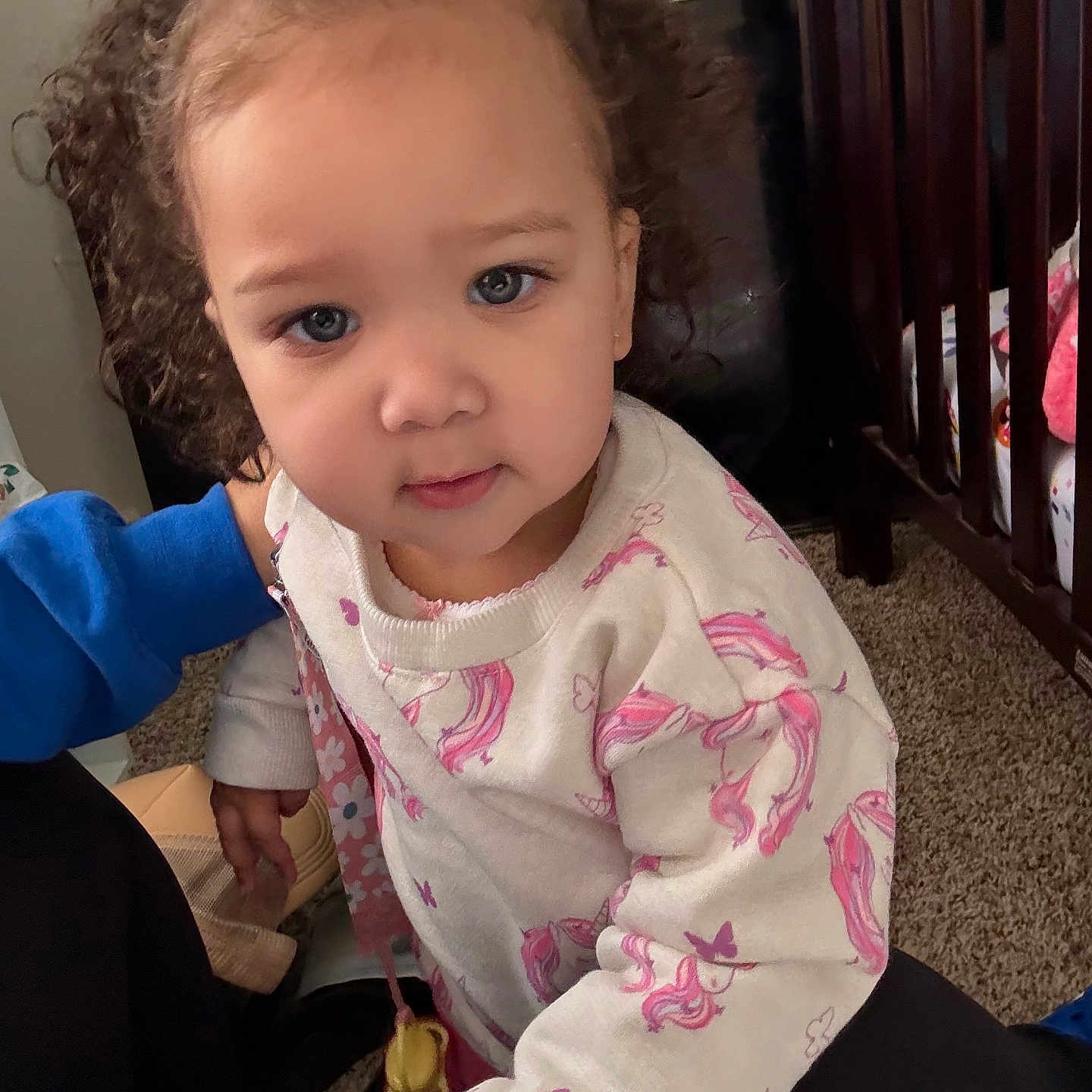 Brooklynn joined the competition — help win amazing prizes! toddler, child, curly_hair, white_bow, sweater, unicorn_print, indoor, carpet, crib, person, blue_clothing, curious, face, portrait, young_child, hand, cute, home, baby, pink