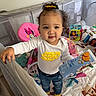 Brooklynn is registered to the contest to win money with this photo: toddler, child, curly_hair, yellow_bow, white_shirt, blue_jeans, socks, playpen, toys, container, gerber_puffs, minnie_mouse, pink_chair, indoor, floor, blanket, baby_toys, smiling, person, cute