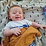 baby, smiling, blanket, grass, outdoor, child, happy, clothing, face, person, pattern, blue_stripes, white_shirt, mustard_cloth, pacifier, hand, skin, head, ear, lying_down