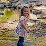 child, toddler, girl, smiling, portrait, outdoor, creek, water, stream, rocks, nature, park, floral_dress, jeans, standing, reflection, sunlight, trees, pebbles, happy