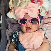 Elaine is registered to the contest to win money with this photo: baby, infant, child, stroller, sunglasses, pink_bow, bib, blanket, portrait, sitting, open_mouth, fashion, cute, outdoor, patterned_clothing, blue_dress, cozy, face, hands, photography