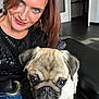 woman, dog, pug, selfie, indoor, couch, smile, blue_eyes, casual_clothing, black_sweater, jeans, short_hair, earring, pet, animal, leather_furniture, home_interior, door, floor, relaxed