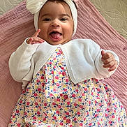 Lilia participe au concours pour gagner de l'argent avec cette photo : baby, bright, buttoned_dress, child, cozy, cute, floral_dress, hand_gesture, happy, headband, indoors, infant, lying_down, pink_quilt, playful, portrait, smiling, soft_texture, tongue_out, white_clothing