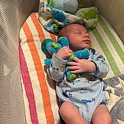 Elias is registered to the contest to win money with this photo: baby, sleeping, crib, blanket, plush_toy, stuffed_animal, mesh_sides, infant, clothing, pacifier, colorful, striped, patterned, cozy, resting, cute, child, indoor, soft, peaceful