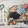 baby, infant, child, smiling, portrait, lying_down, blanket, woodland_animals, animal_print, milestone_photo, monthly_milestone, numbers, handwritten_text, bib, striped_shirt, dark_pants, socks, indoor, cozy, happy