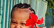Yuhanna participe au concours pour gagner de l'argent avec cette photo : braids, cheeks, child, closeup, cute, garden, happy, hibiscus_flower, laughing, outdoor, patterned_clothing, portrait, railing, red_flower, sleeveless_dress, smile, sunlight, teeth, toddler, wall