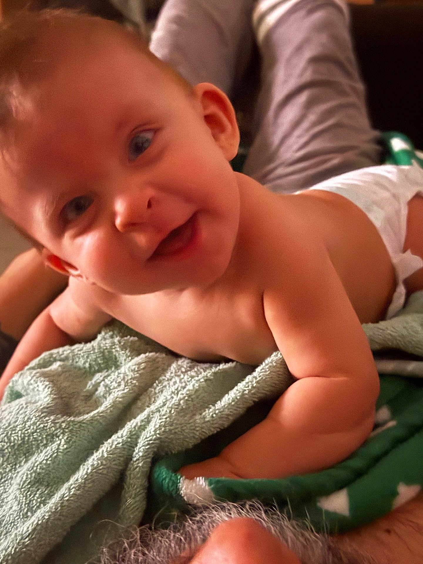 Nymeria is registered to the contest to win money with this photo: arm, baby, blanket, child, closeup, cozy, curious, cute, diaper, face, happy, indoors, infant, lying_down, person, portrait, skin, smiling, soft_lighting, towel