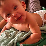 Nymeria is registered to the contest to win money with this photo: baby, smiling, towel, skin, face, arm, blanket, happy, infant, cute, lying_down, indoors, child, person, closeup, soft_texture, warm_lighting, expression, portrait, relaxing