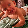 baby, smiling, towel, skin, face, arm, blanket, happy, infant, cute, lying_down, indoors, child, person, closeup, soft_texture, warm_lighting, expression, portrait, relaxing
